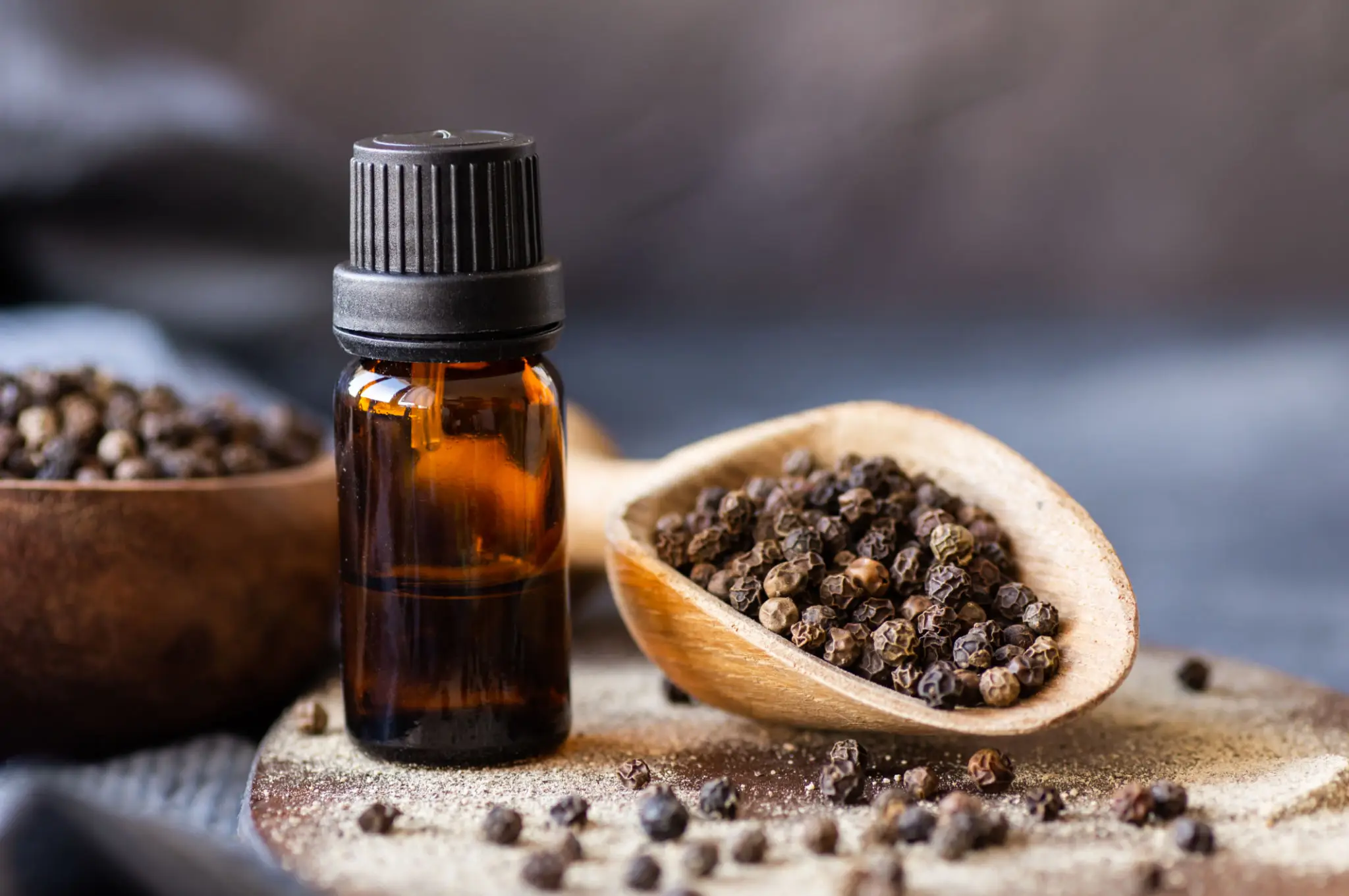 A bottle of black pepper essential oil beside a spoon of peppercorns