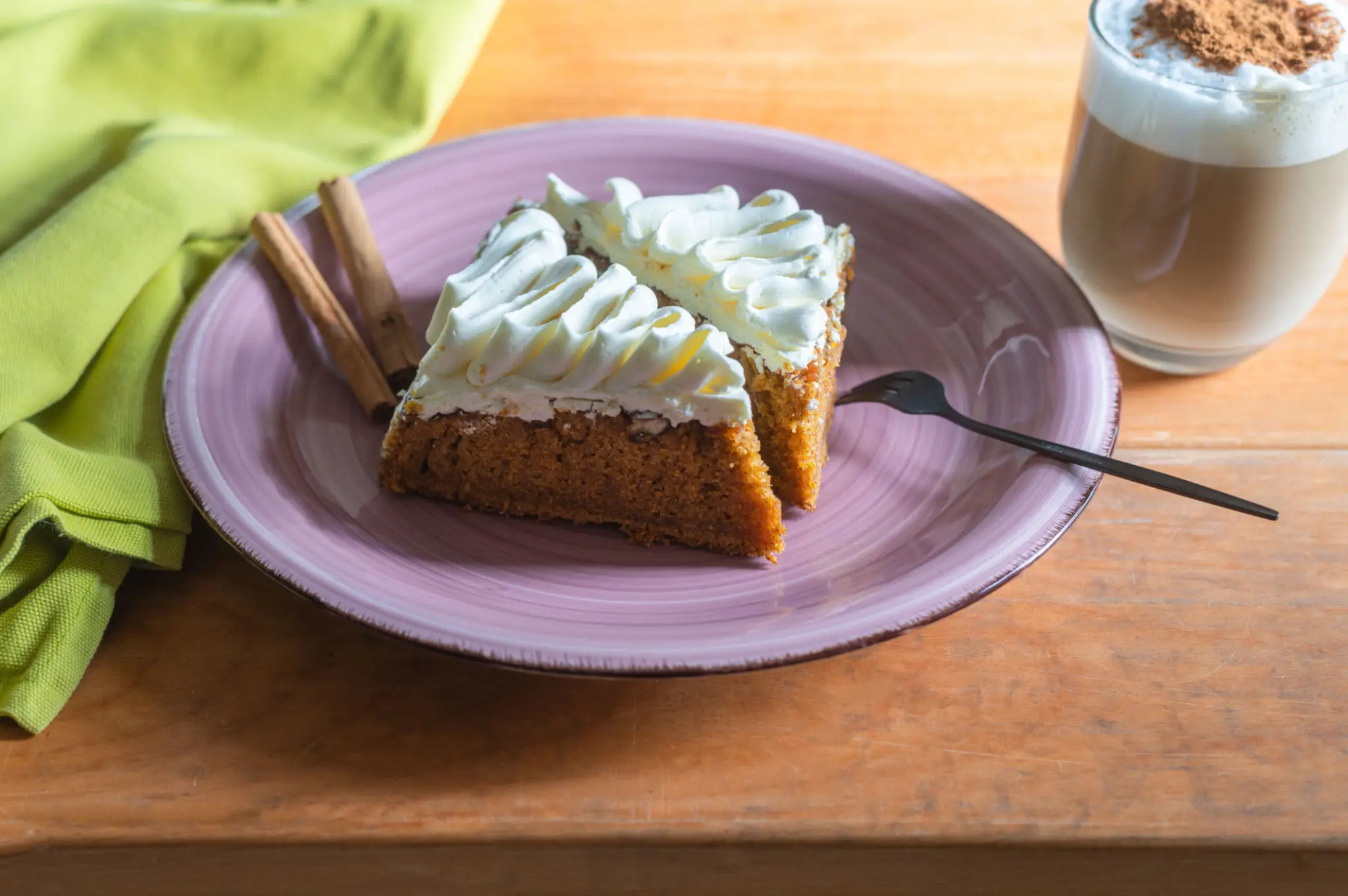 A slice of carrot cake with cream cheese icing beside a cinnamon latte