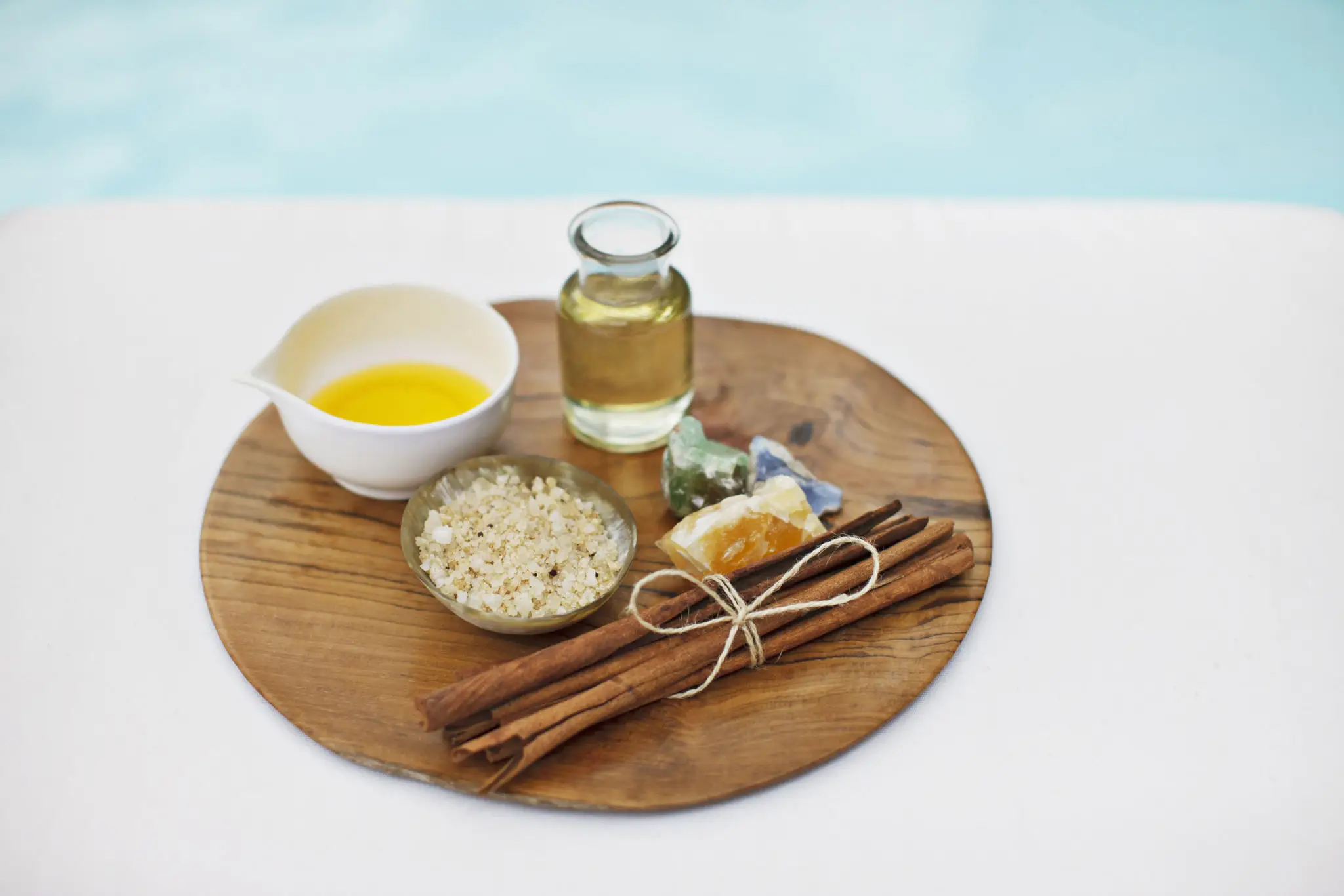 A small bottle of golden essential oil on a round board with cinnamon quills and a dish of oil