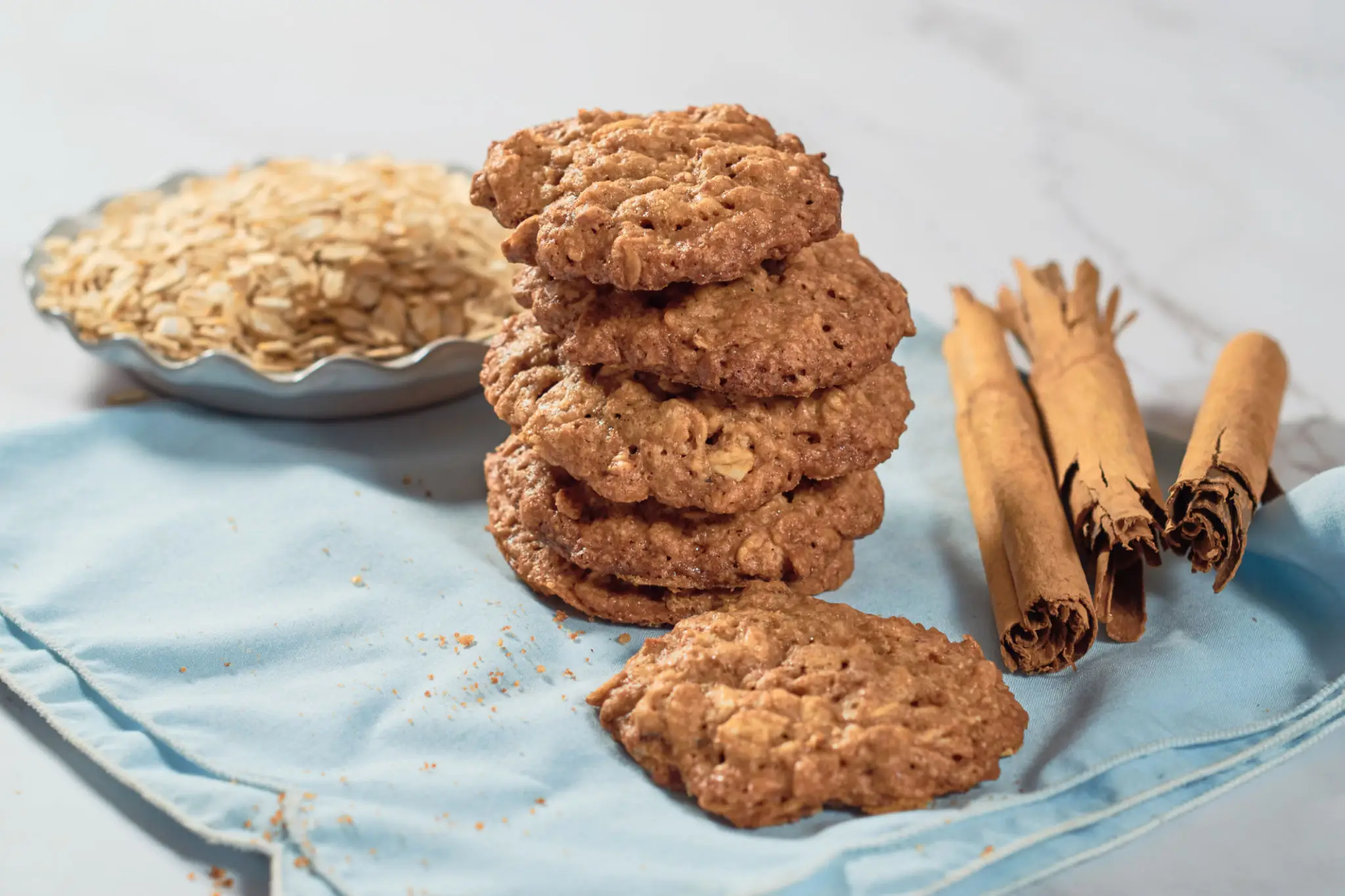 A stack of soft oatmeal biscuits with rolled oats and cinnamon quills alongside