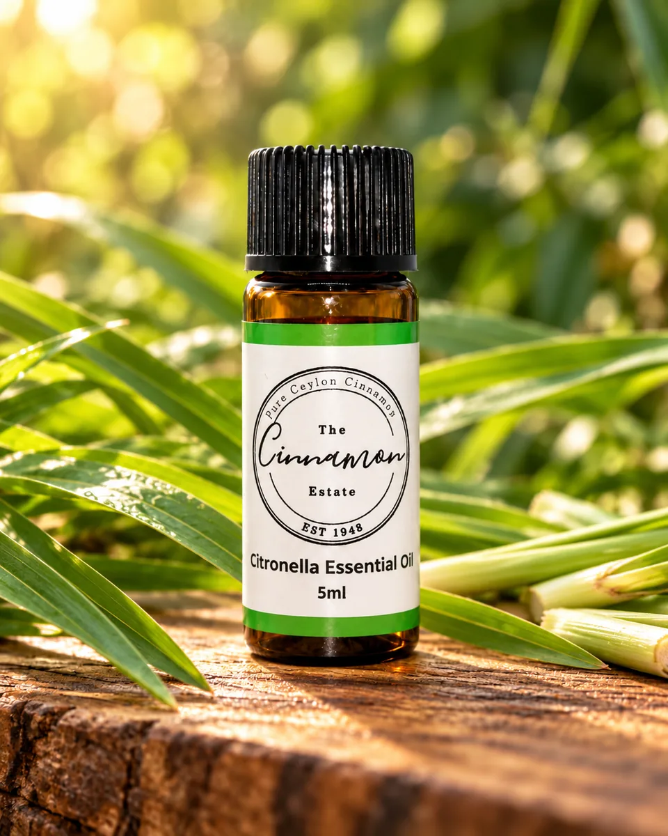 An amber dropper bottle of The Cinnamon Estate citronella essential oil, with a bright green striped label, on a weathered wooden board among long grass blades.